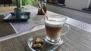 A glass mug of coffee with a red and white straw, a glass plate with cookies, and a cactus plant in the background.