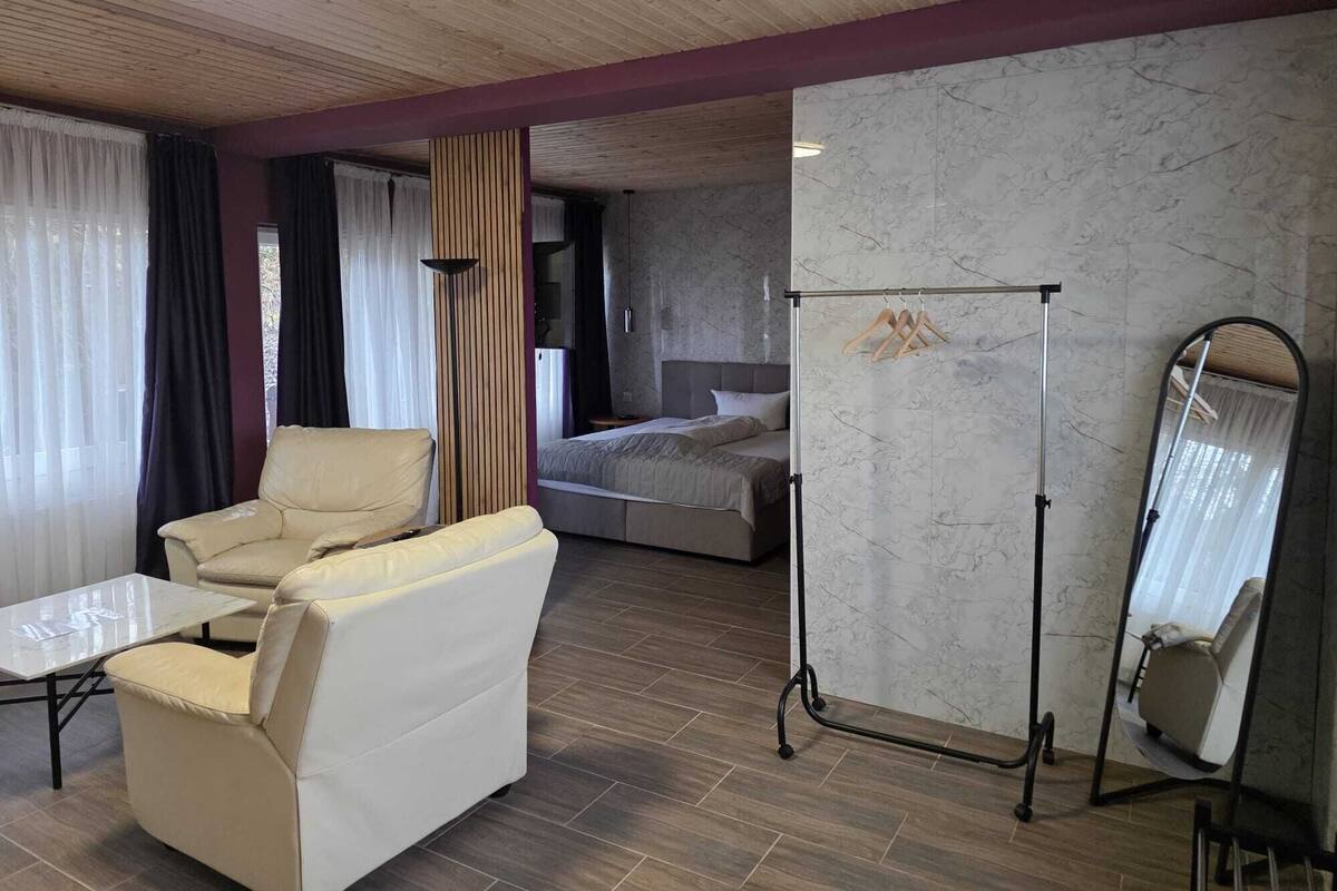 Una habitación de hotel moderna con sofá, cama, espejo y perchero.