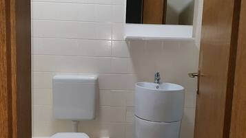 Un baño pequeño y limpio con azulejos blancos, un inodoro, un lavabo y un espejo sobre el lavabo.