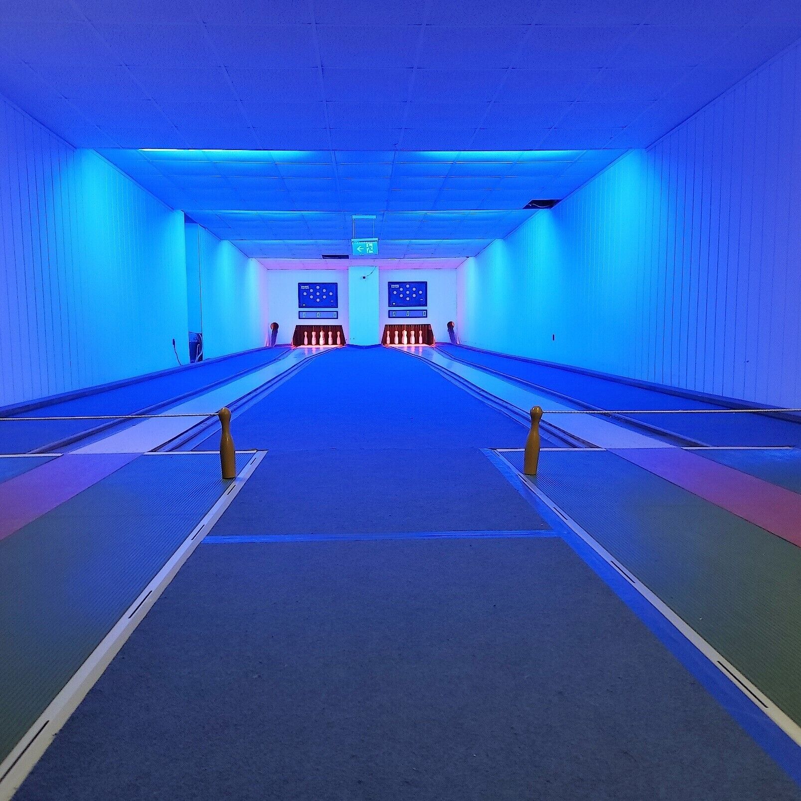 Une salle de bowling avec plusieurs pistes, une allée centrale et un panneau de contrôle à l’extrémité.
