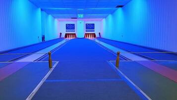 Une salle de bowling avec plusieurs pistes, une allée centrale et un panneau de contrôle à l’extrémité.