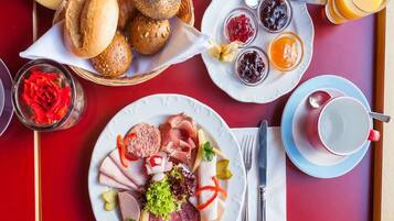 A breakfast setting with various food items, including bread, jams, and meats, on a red table.