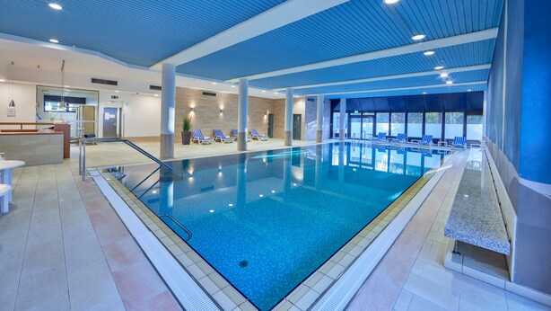 Une piscine intérieure à l’eau d’un bleu cristallin, entourée de chaises longues et d’un espace d’accueil doté d’un comptoir.