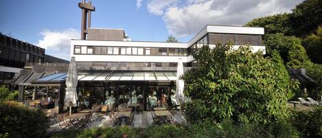 Un edificio moderno con techo plano, amplios ventanales y un patio central con mesas al aire libre.