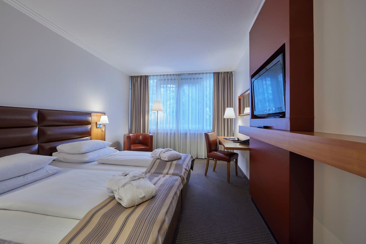 A hotel room with two beds, a desk, a chair, a television, and a window with curtains.