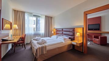 Une chambre d’hôtel avec un grand lit, deux tables de chevet avec des lampes, un bureau avec une chaise, une télévision et un fauteuil rouge.