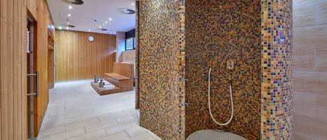 A modern spa with a mosaic-tiled shower area, wooden walls, and a tiled floor.