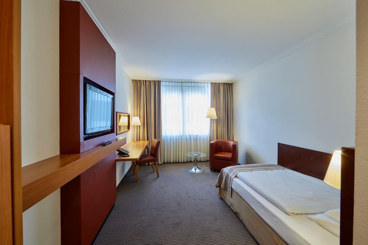 A hotel room with a bed, a desk, a chair, a TV, and a window with curtains.