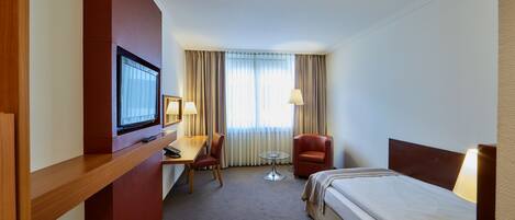 A hotel room with a bed, a desk, a chair, a TV, and a window with curtains.