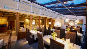 Un restaurant doté d’une salle à manger, de hauts plafonds et d’un toit en verre. Les tables sont dressées avec des nappes blanches et agrémentées de centres de table.