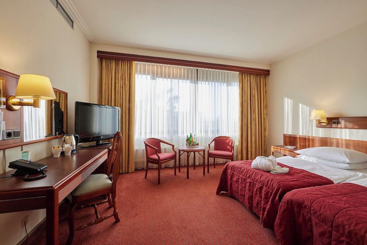 A hotel room with a bed, a desk with a computer, a television, two chairs, a small table, and a window with curtains.