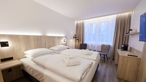 Une chambre d’hôtel avec un grand lit, des tables de chevet, une chaise, un bureau et un téléviseur.