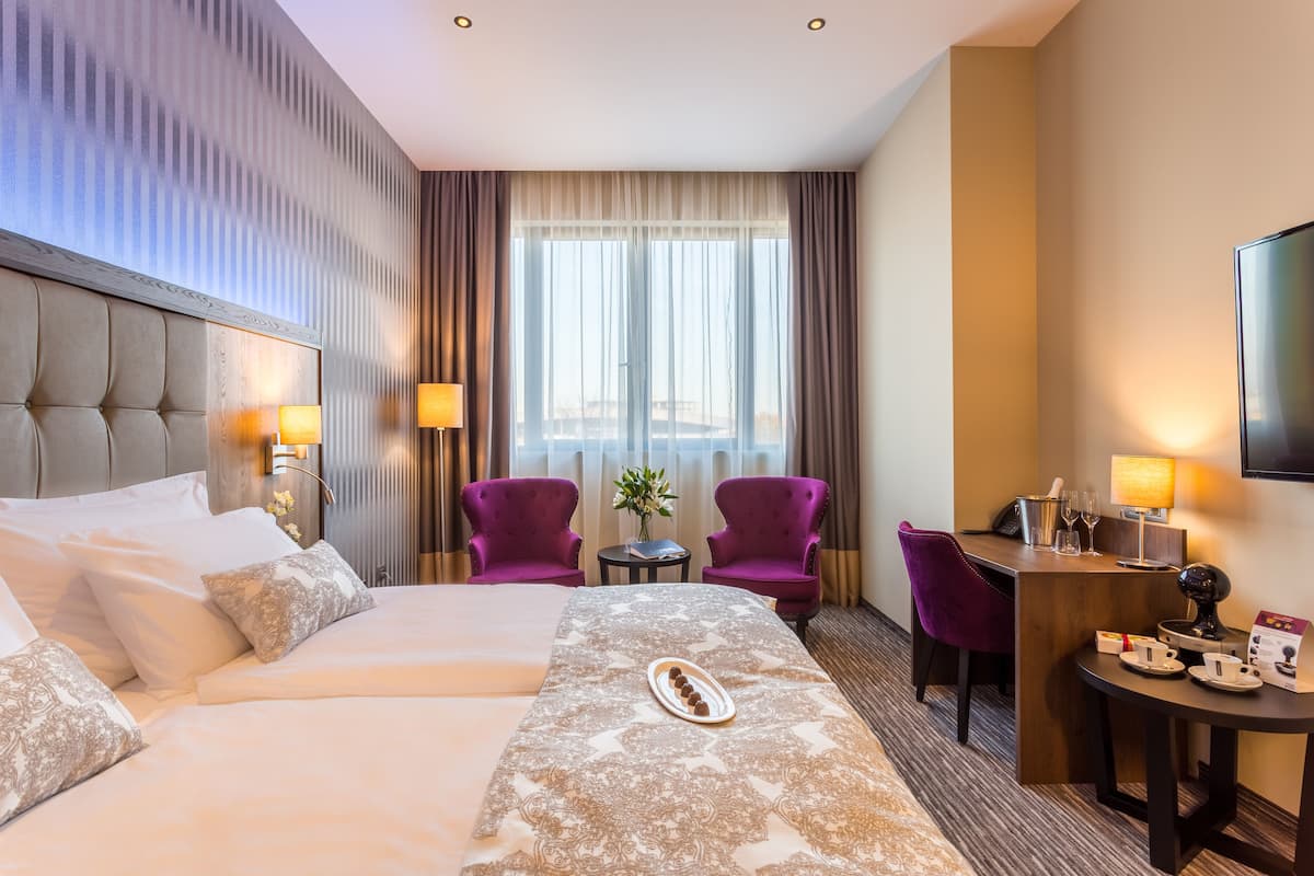Une chambre d’hôtel avec un grand lit, deux fauteuils, un bureau avec une lampe et une petite table avec un service à thé.