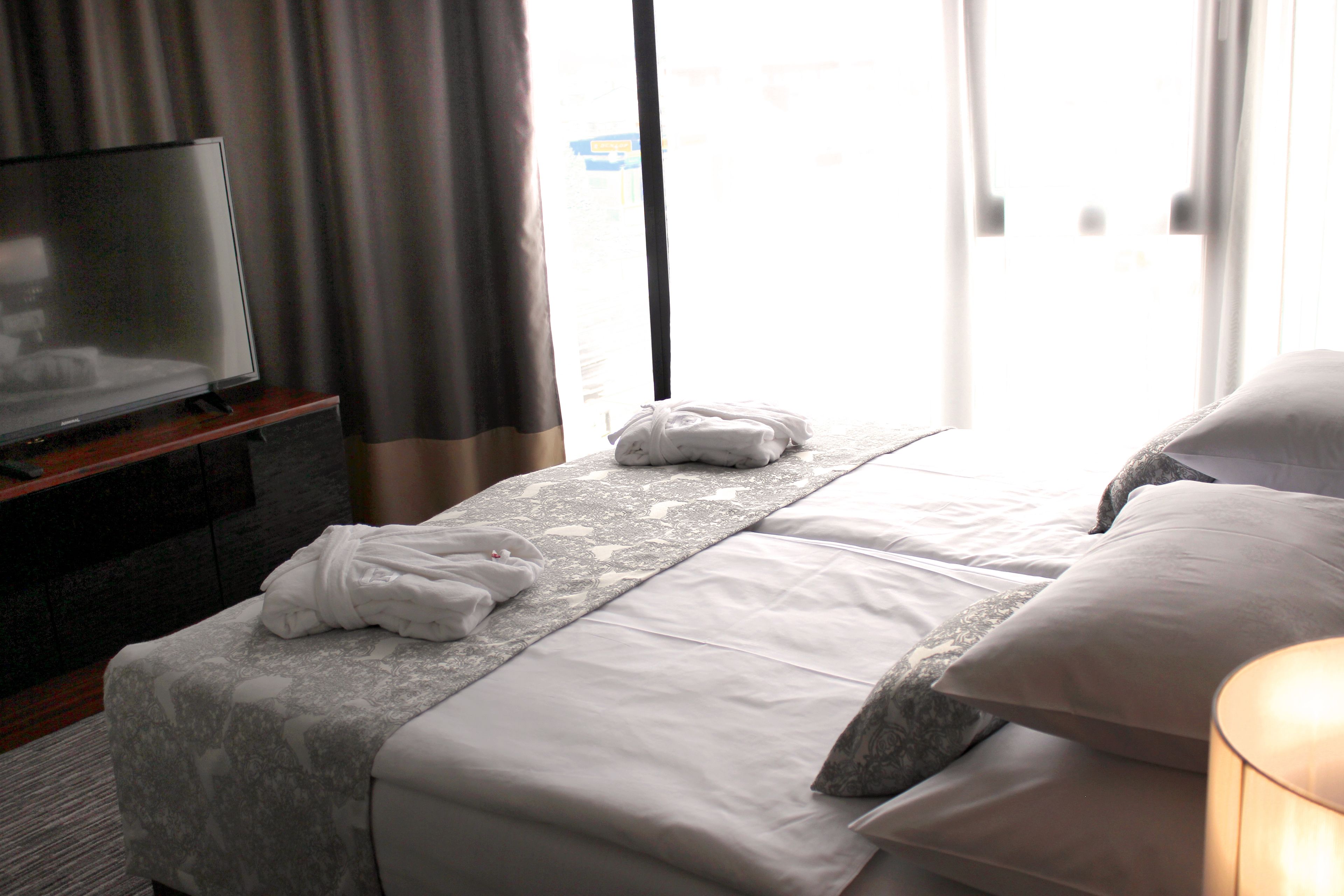 A hotel room with a bed, a TV, and a window with curtains.