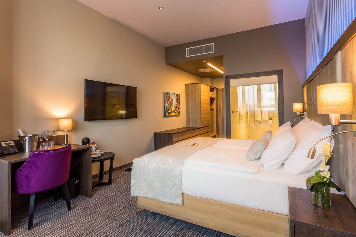 Une chambre d’hôtel avec un lit, un bureau, une chaise, une télévision, un tableau et une lampe.