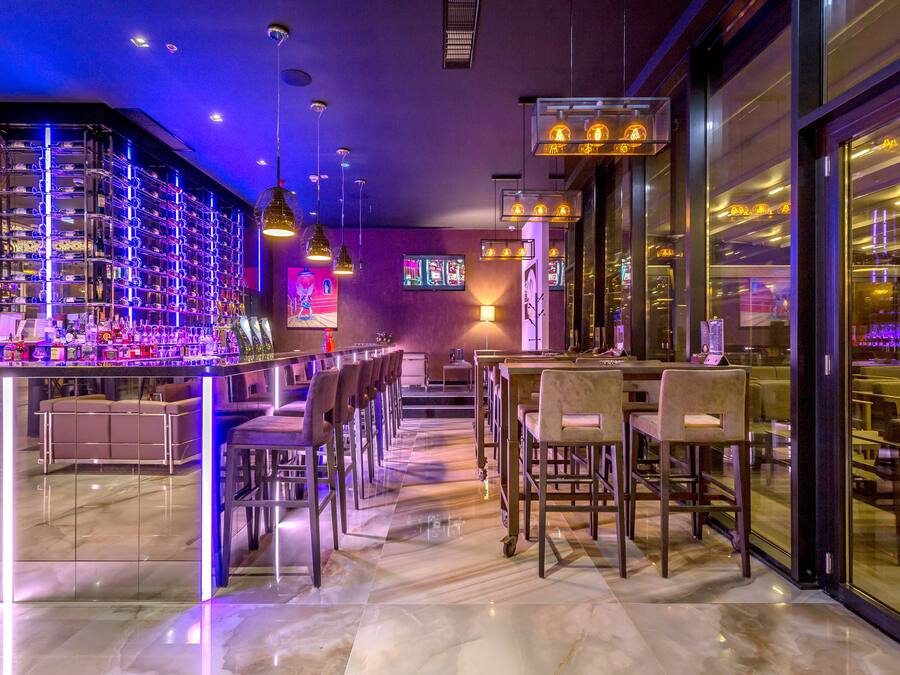 Een moderne bar met een marmeren vloer, verschillende zithoeken en sfeerverlichting.