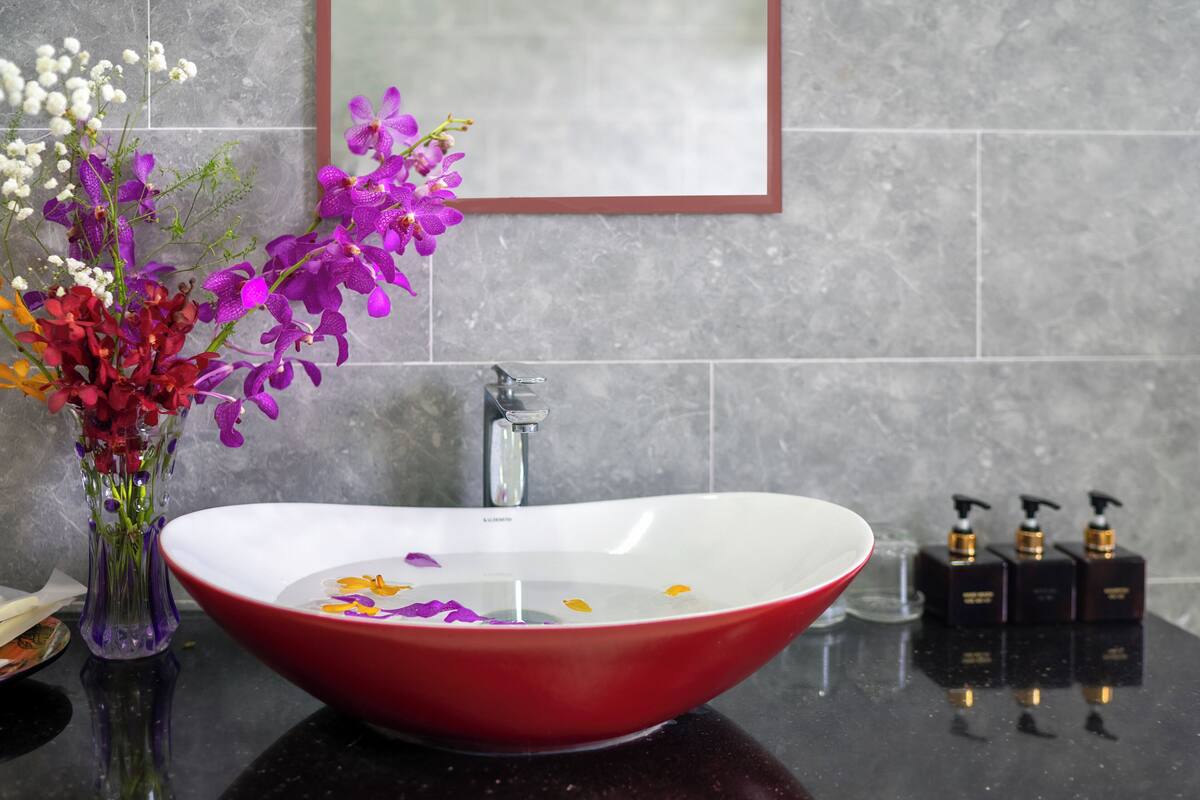 A bathroom with a red sink, a vase of flowers, and a mirror.