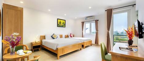 A hotel room with a bed, a desk, a chair, a small table, a vase with flowers, and a window with curtains.