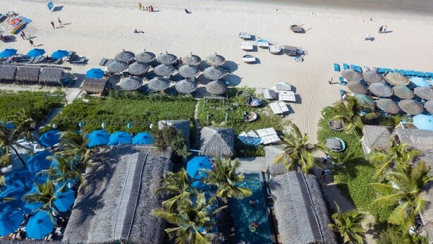 An aerial view of a beach resort with a swimming pool, lounge chairs, umbrellas, and palm trees. - Yellow Daisy Villa (Da Nang)