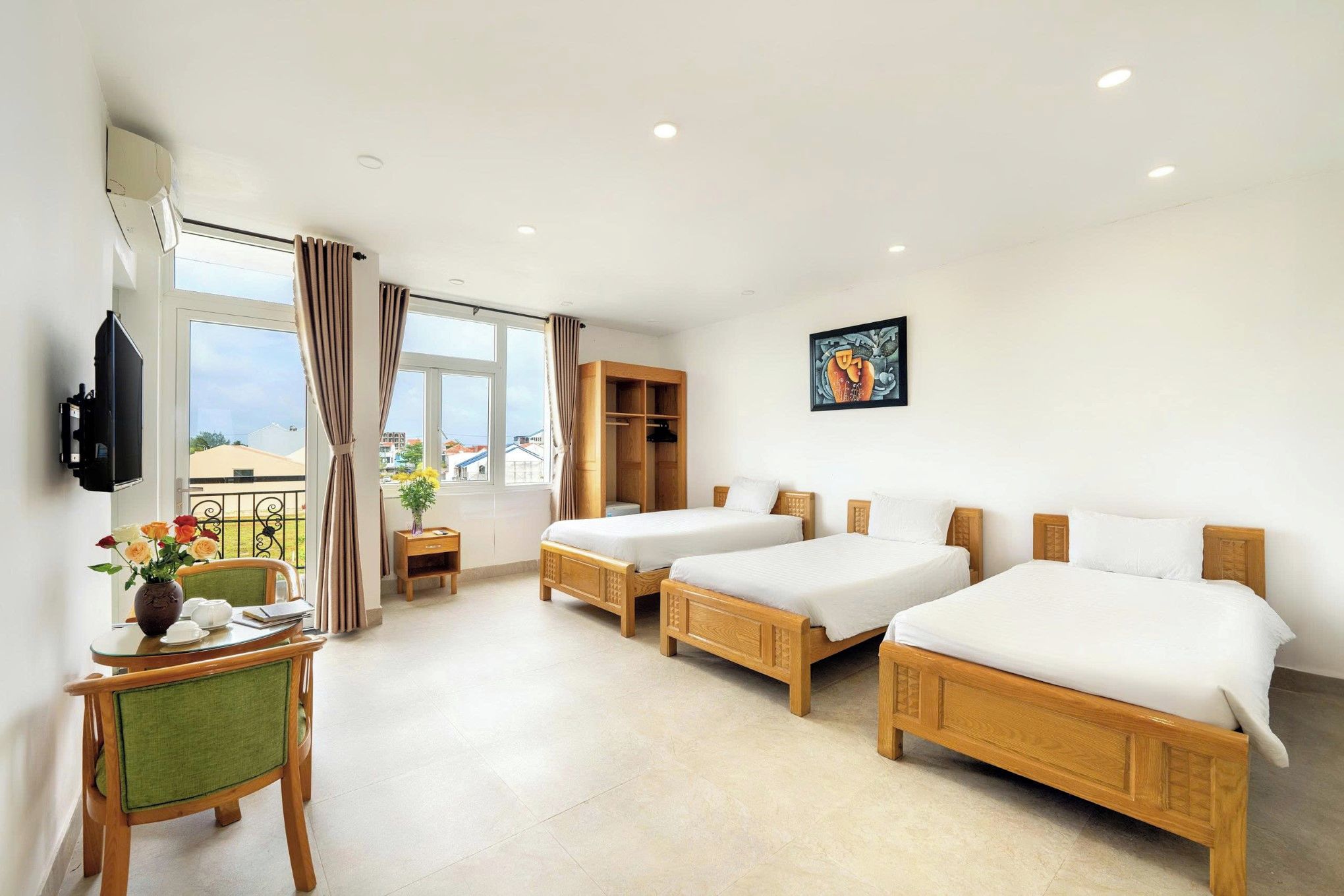 A hotel room with two wooden beds, a desk with a chair, a small table with a vase of flowers, and a painting on the wall.