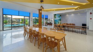 A spacious indoor area with a large wooden table and chairs, a ceiling with recessed lighting, and large windows offering a view of an outdoor pool. - Yellow Daisy Villa (Da Nang)