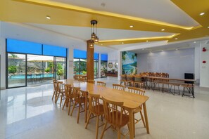 A spacious indoor area with a large wooden table and chairs, a ceiling with recessed lighting, and large windows offering a view of an outdoor pool. - Yellow Daisy Villa (Da Nang)
