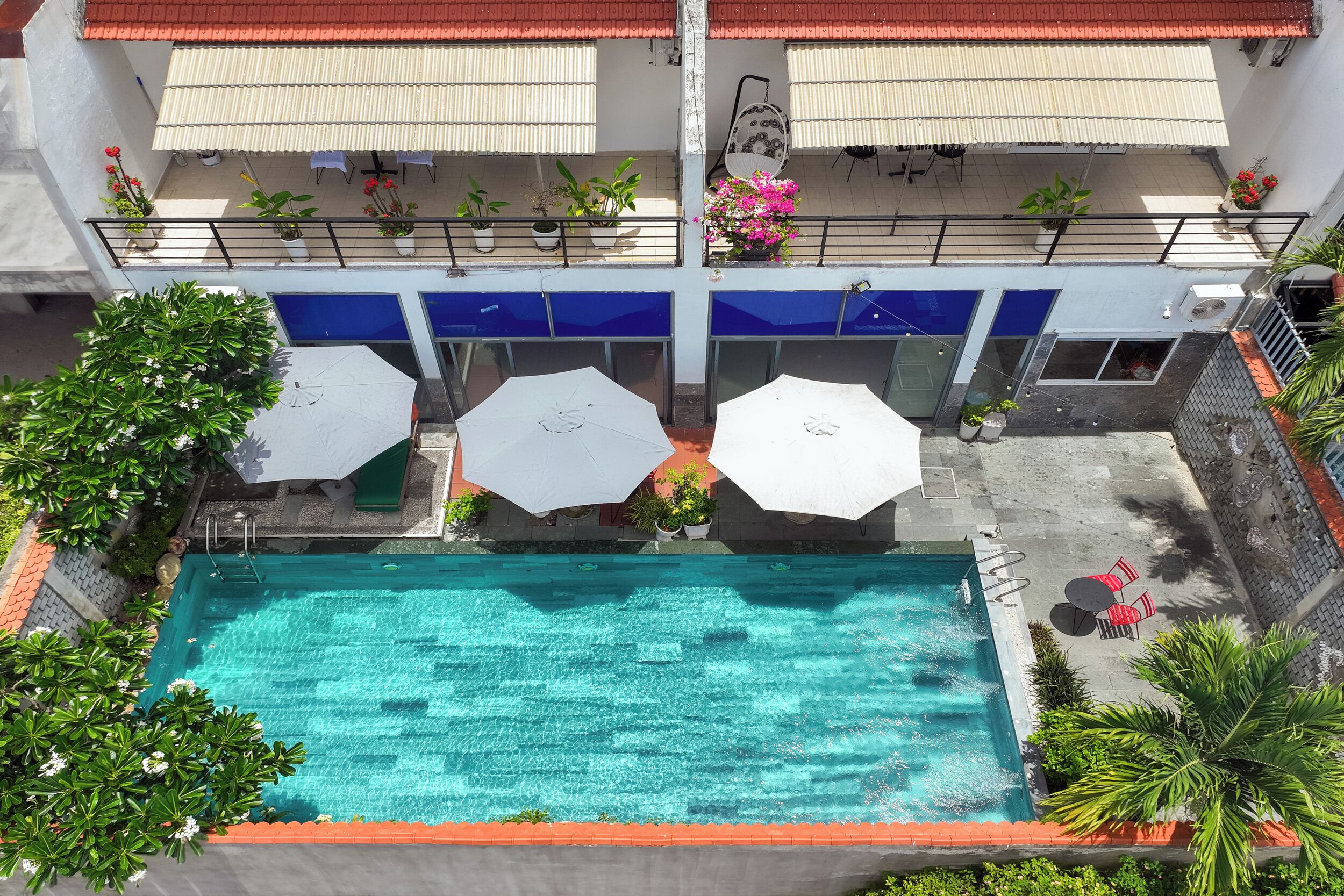 An aerial view of a hotel with a swimming pool, outdoor seating, and potted plants.