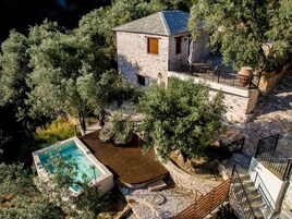 A stone house with a pool, surrounded by trees and a stone staircase.