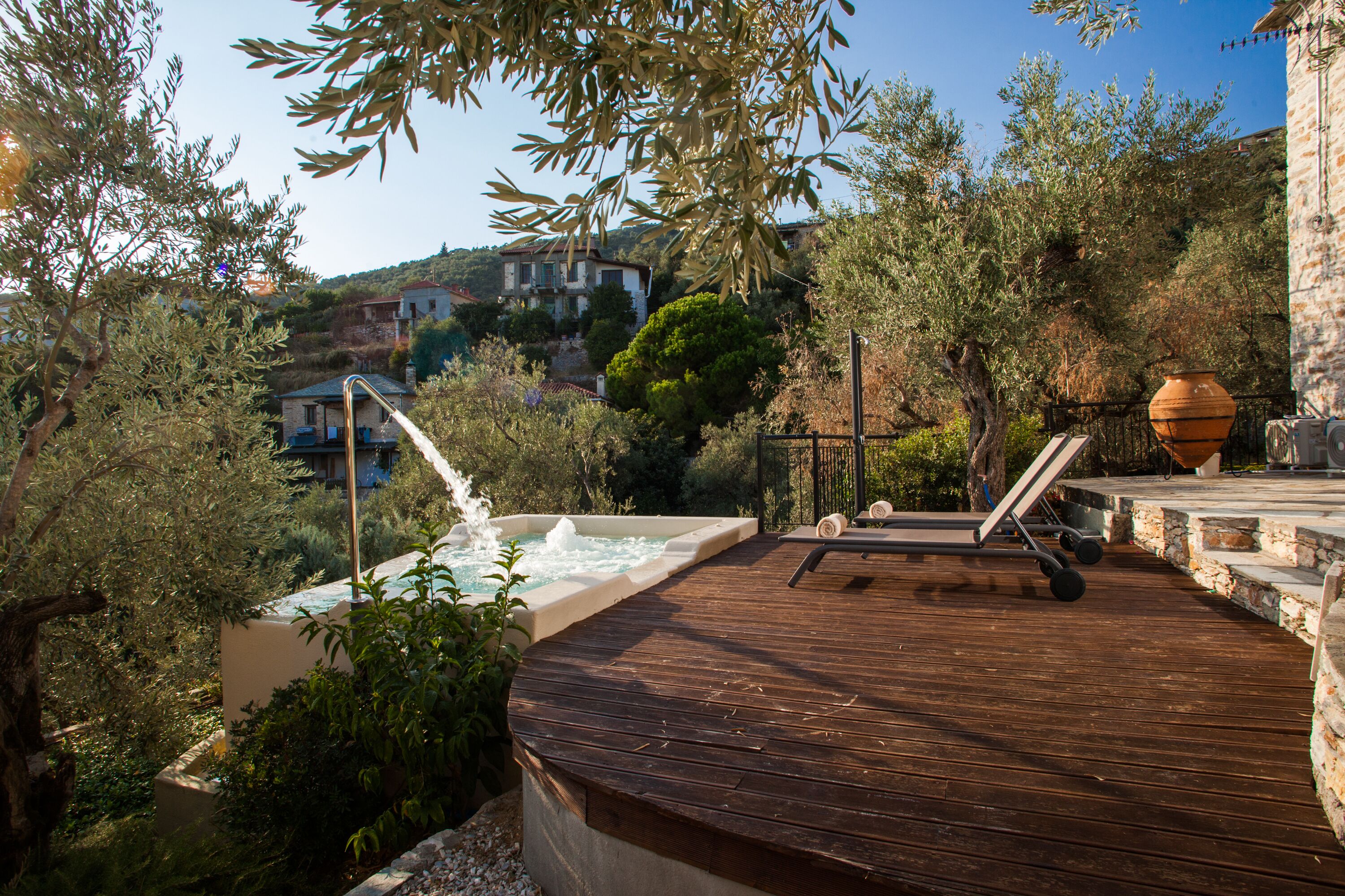 A wooden deck with a hot tub, lounge chairs, and a stone wall.