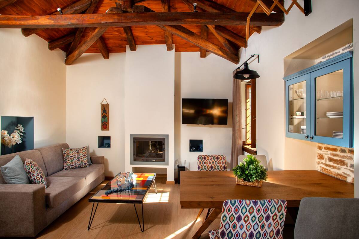A living room with a wooden ceiling, a sofa, a coffee table, a fireplace, and a dining area with a table and chairs.
