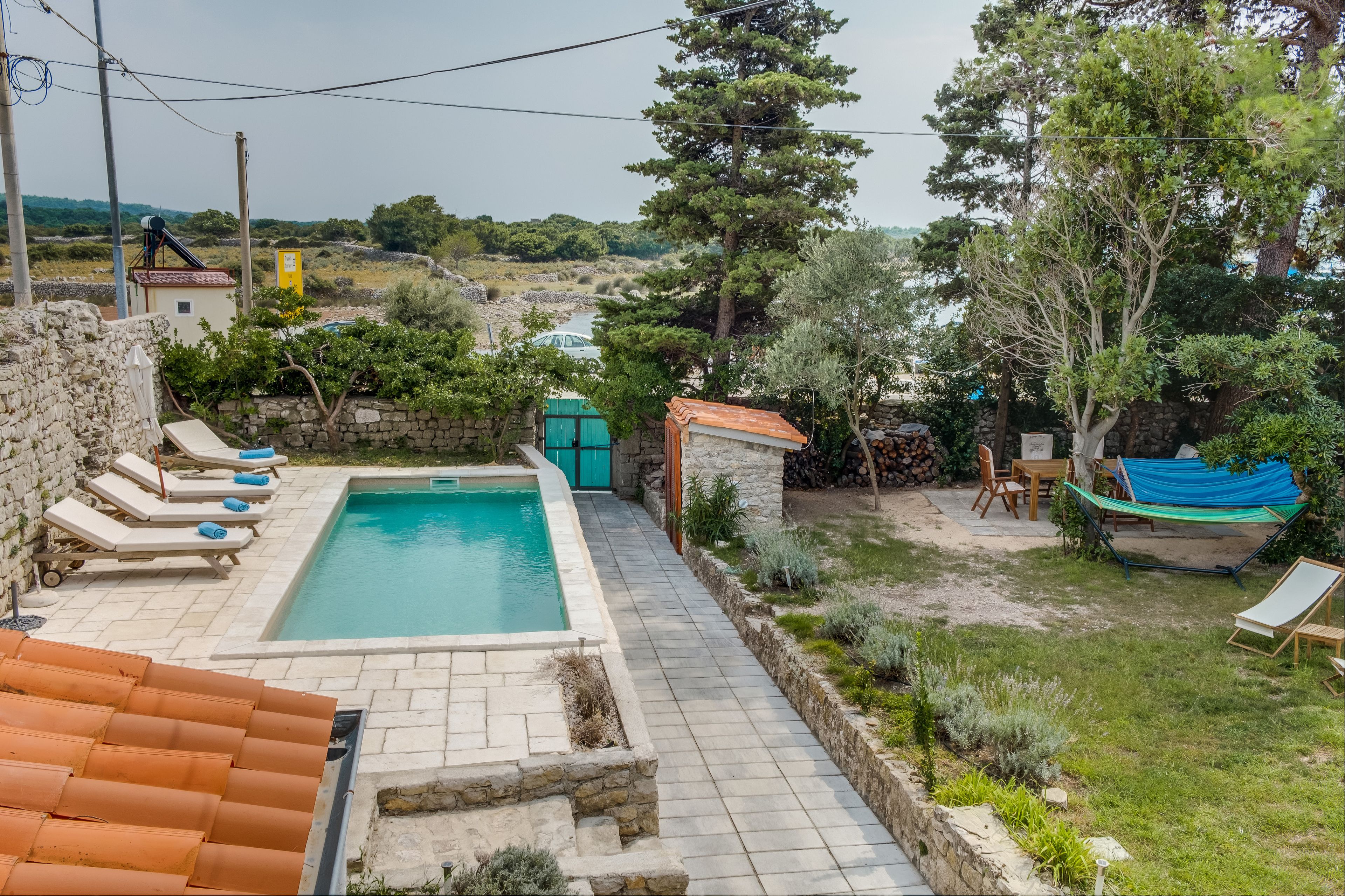 A pool area with lounge chairs, a small building, and a hammock.