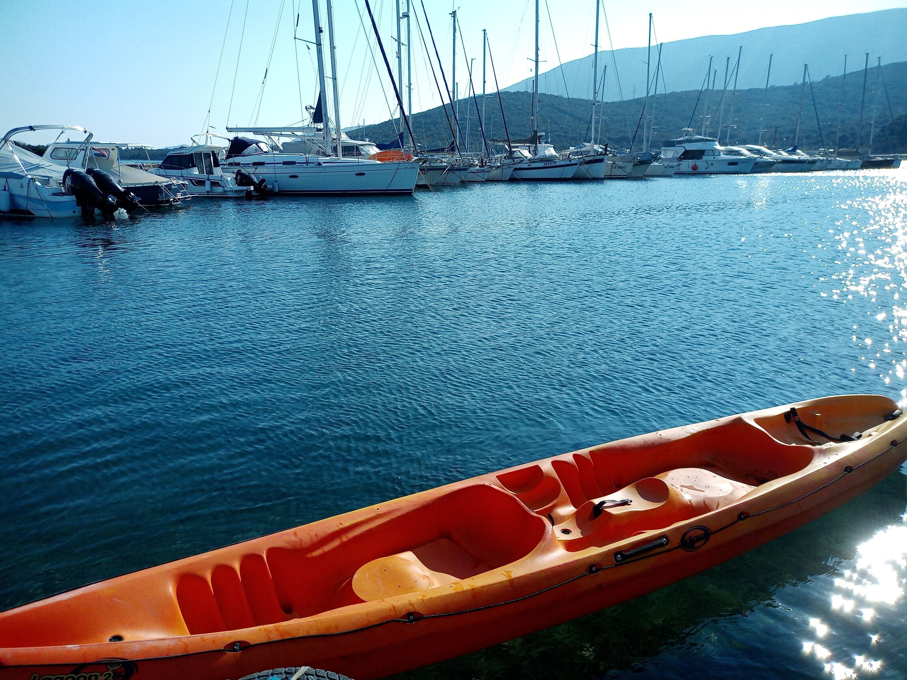 Ein Hafen mit mehreren Segelbooten an den Liegen und einem roten Kajak im Vordergrund.