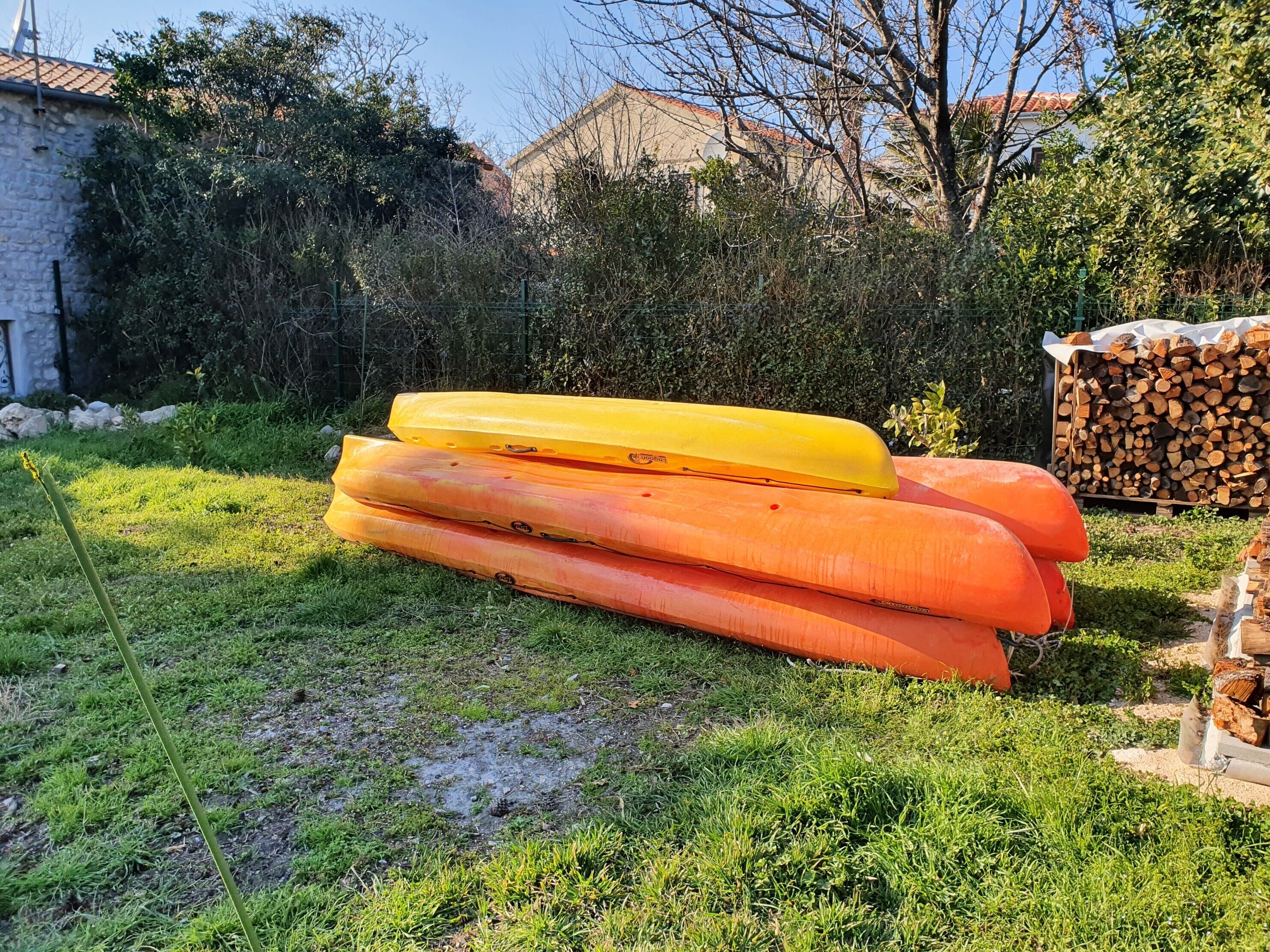 A grassy area with three kayaks stacked on the ground.
