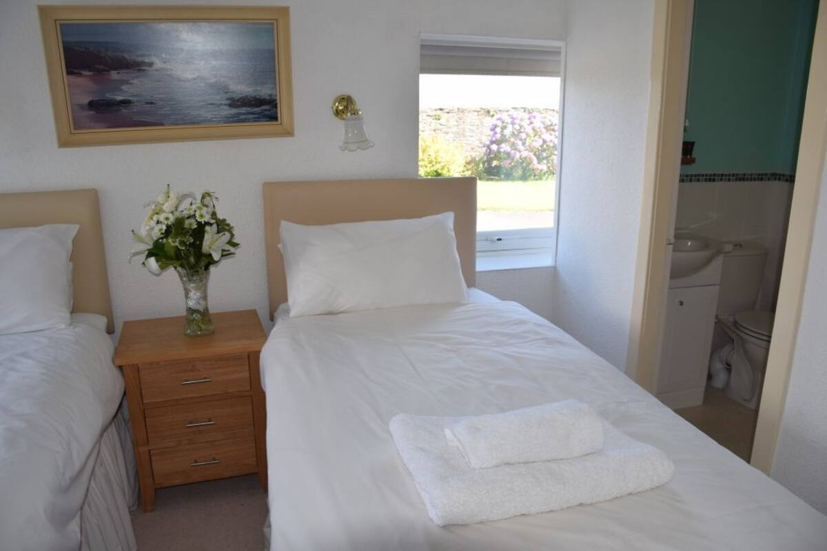 A bedroom with a bed, a nightstand, a vase with flowers, a painting on the wall, and a window with a view of the outdoors.