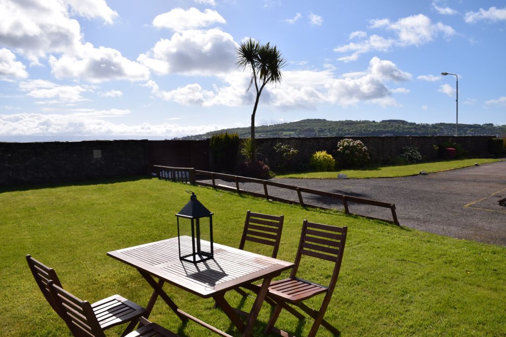 A grassy outdoor area with a table and chairs, a lamp, and a view of a hill in the background.