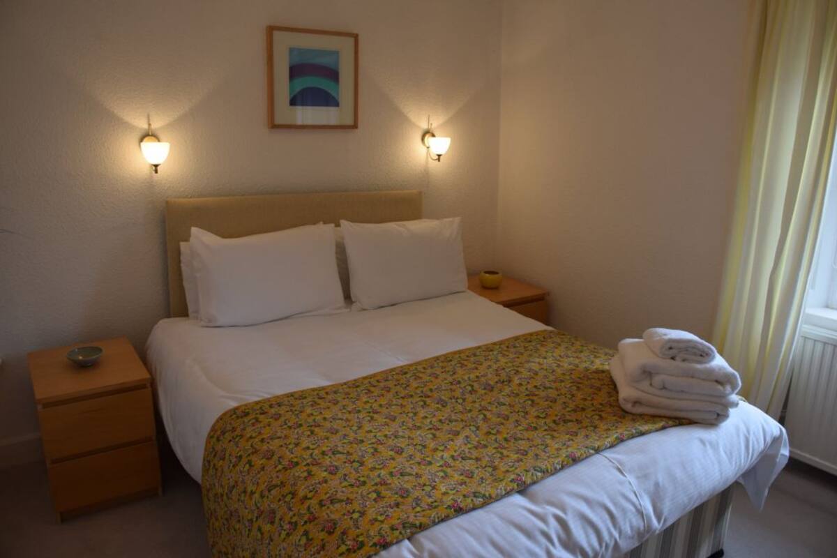 A neatly made bed with a floral bedspread, two bedside lamps, a small bedside table with a bowl, and a framed picture on the wall.
