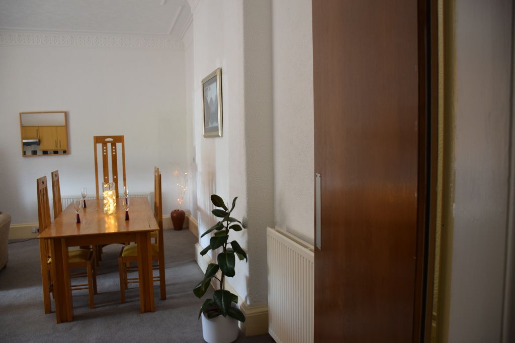 A dining area with a wooden table and chairs, a potted plant, a radiator, and a framed picture on the wall.