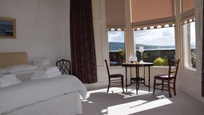 A hotel room with a bed, a table with chairs, and a view of the sea. - One Marine Place (Rothesay)