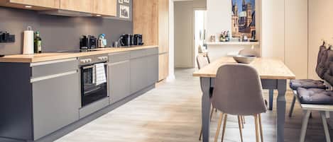 A modern kitchen with grey cabinets, wooden countertops, and a dining area with a wooden table and chairs.