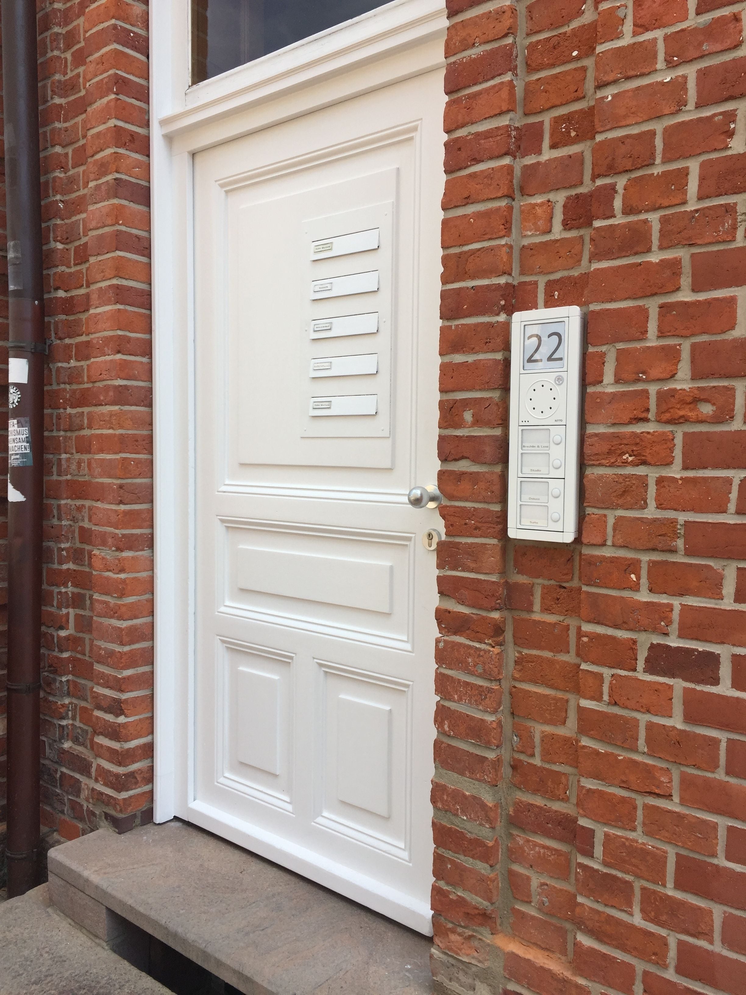A white door with a keypad lock, a mailbox, and a number plate on a brick wall.