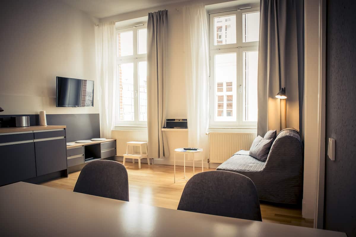 Ein modernes Wohnzimmer mit einer Couch, einem Esstisch und einem an der Wand montierten Fernseher.