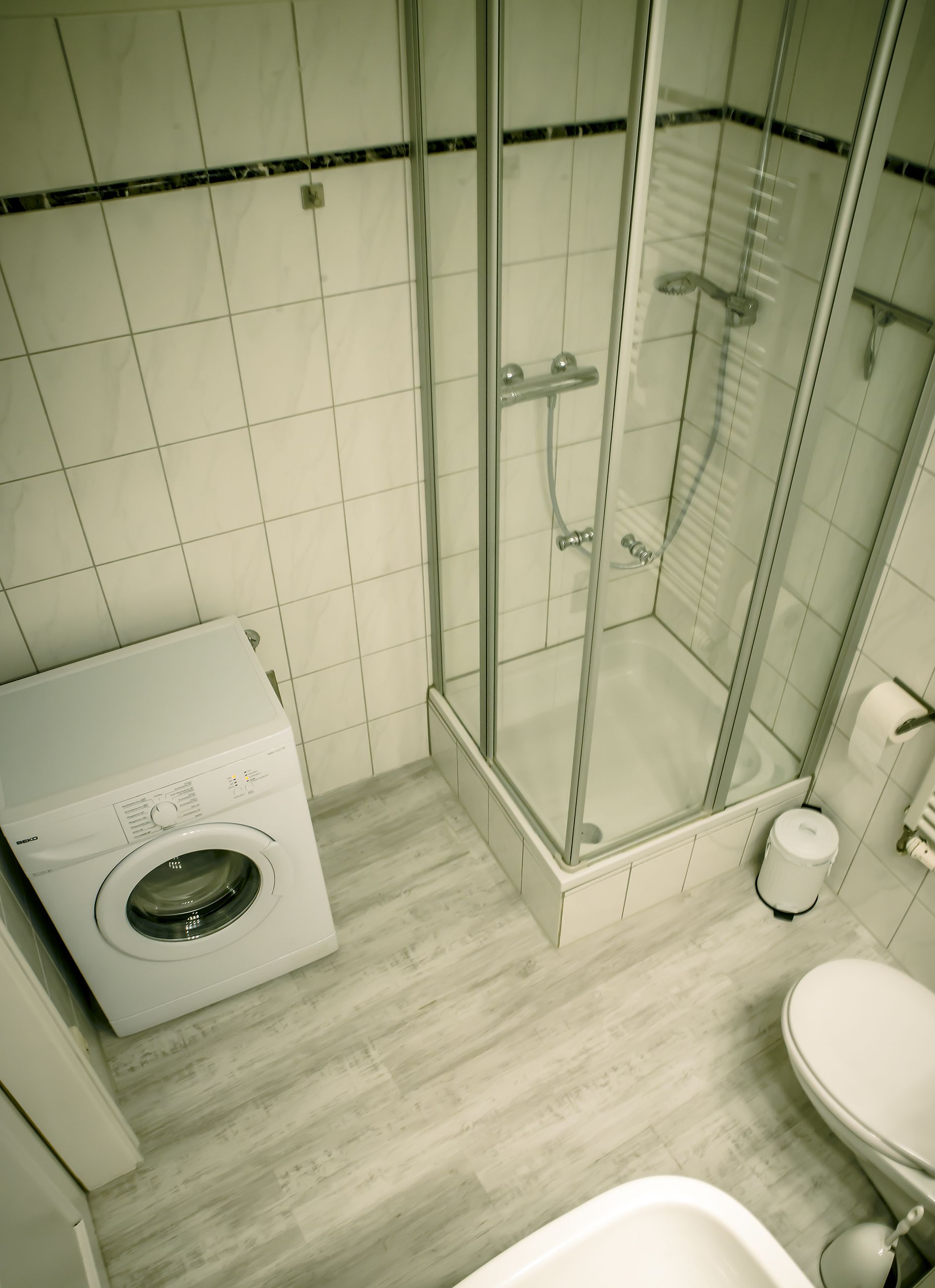 A bathroom with a glass-enclosed shower, a washing machine, and a toilet.
