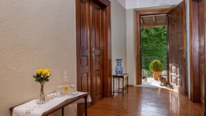 A hallway with wooden doors, a table with a vase of yellow flowers, and a potted plant visible through an open door.