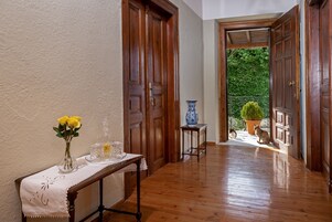 Un pasillo con puertas de madera, una mesa con un jarrón de flores amarillas y una planta en maceta visible a través de un umbral abierto.