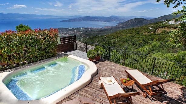 A hot tub on a wooden deck with a view of the sea and hills.