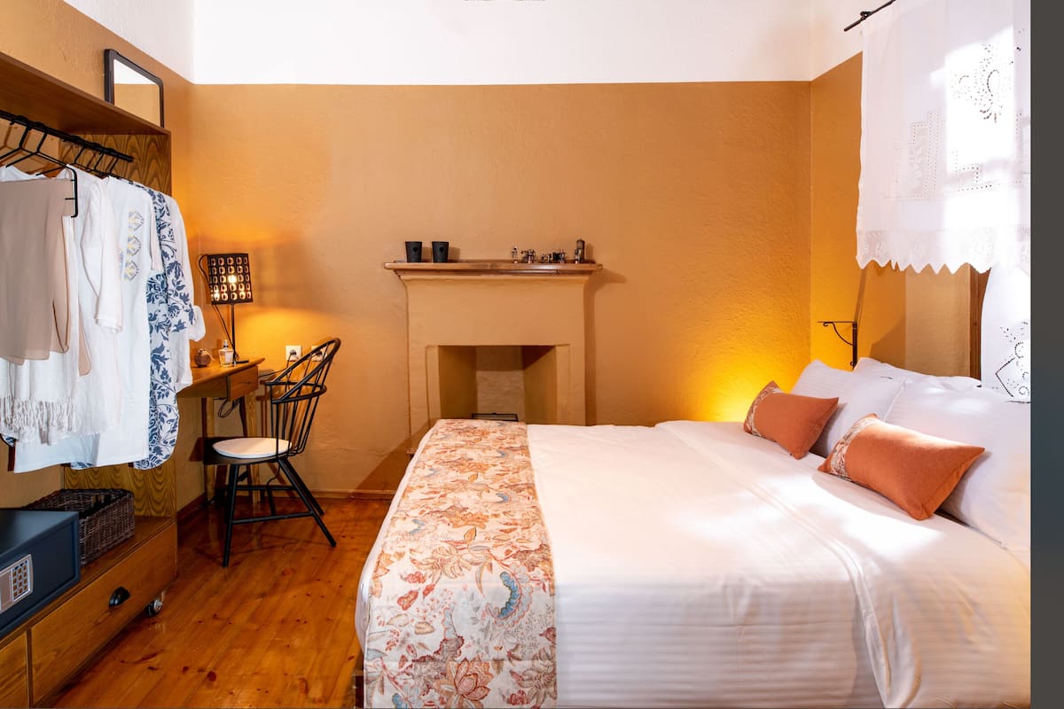 A bedroom with a bed, a chair, a dresser, a mirror, and a fireplace.