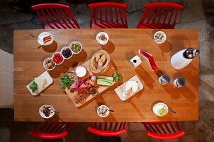 Una mesa de madera con diversos alimentos y utensilios, rodeada de sillas rojas.