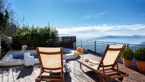 A wooden deck with two lounge chairs, a hot tub, and a small table with a watermelon and other items.