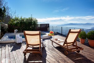 Una terraza de madera con dos sillones de descanso, un jacuzzi y una mesa pequeña con sandía y otros objetos.