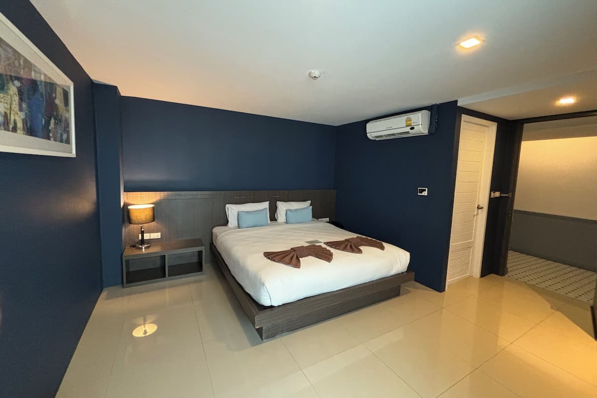 A modern hotel room with a large bed, bedside table, and a wall-mounted air conditioner.